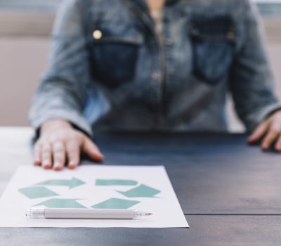 person-showing-recycle-paper-with-pen-wooden-table